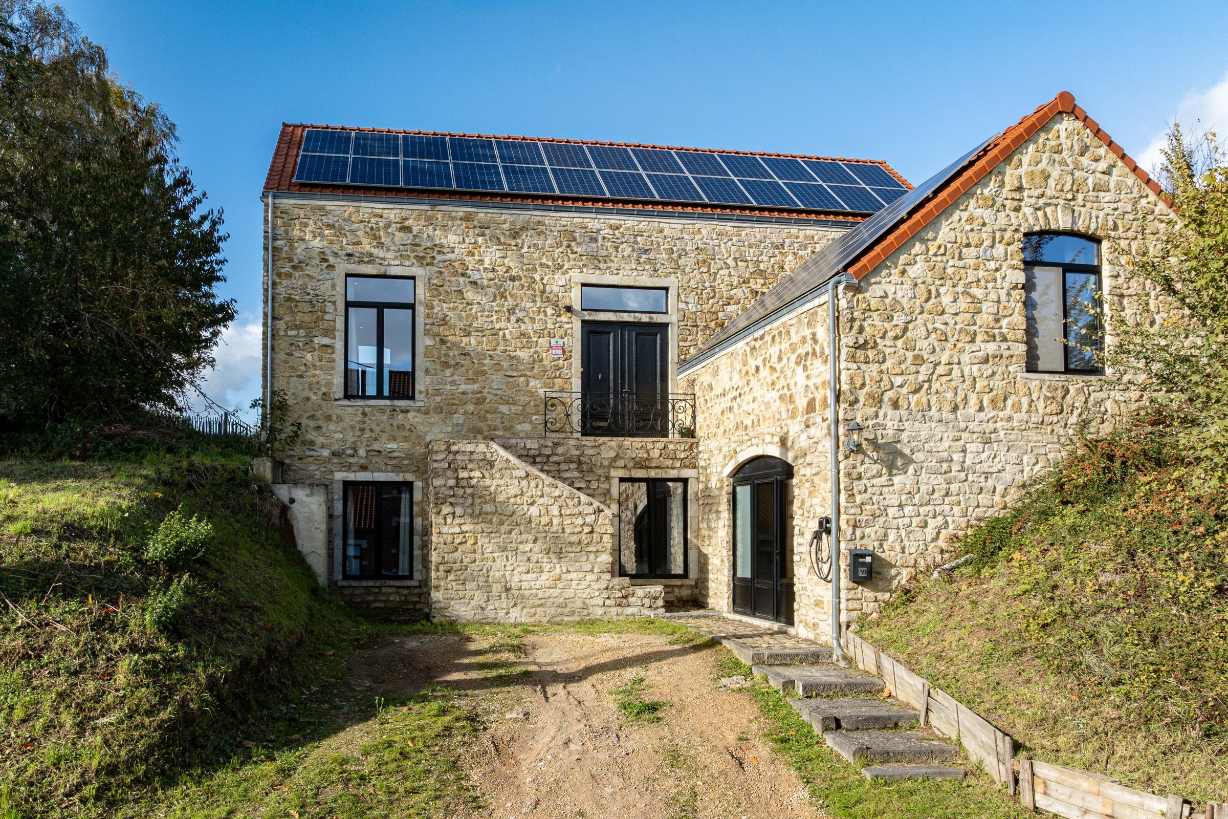La grange en pierre vue depuis le chemin, panneaux solaires sur la toiture